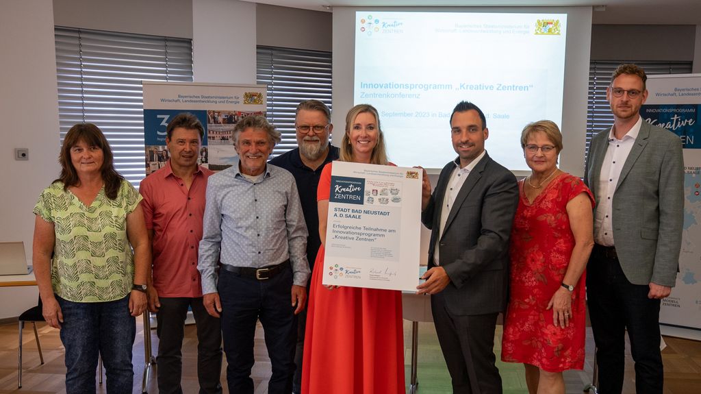 Staatssekretärin Anna Stolz übergibt stellvertretend für Wirtschaftsminister Hubert Aiwanger die Teilnahmeurkunde an Michael Werner, Erster Bürgermeister der Stadt Neustadt a.d. Saale, und Vertreteinnen und Vertreter des Stadtrats. Foto: StMWi