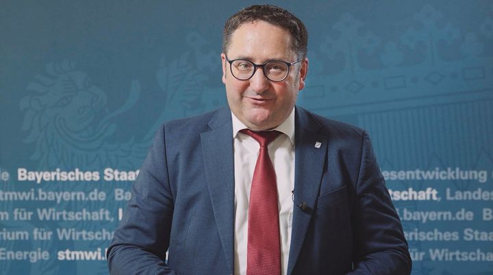  Tobias Gotthardt, Staatssekretär im Bayerischen Staatsministerium für Wirtschaft, Landesentwicklung und Energie, vor einer Leinwand bei der Videobotschaft zum Bayerischen Energiepreis. Hier klicken, um Videobotschaft zu öffnen. 