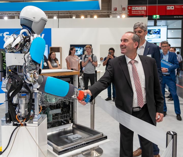Am Stand der DLR begrüßt Aiwanger den anthropomorphen Roboter David, der Gelenke mit variablen Steifigkeitsfaktoren besitzt. (Fotonachweis: StMWi / E. Neureuther)