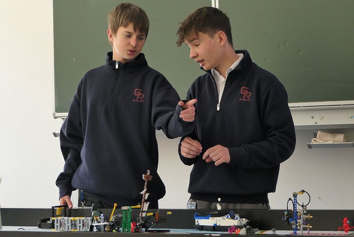 Zwei Personen vor einer Tafel in einem Klassenzimmer.