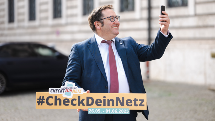 Staatssekretär Tobias Gotthardt hält ein Smartphone in die Luft und wirbt für die Mobilfunk-Messwoche. 