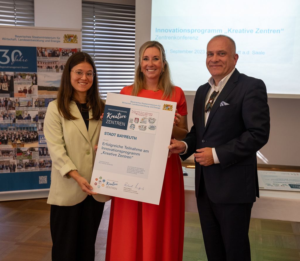 Staatssekretärin Anna Stolz übergibt Bernhard Sippel, stellvertretender Leiter des Amts für Wirtschaftsförderung der Stadt Bayreuth, und Katharina Gogolin (Cima Beratung + Management GmbH) die Teilnahmeurkunde. Foto: StMWi