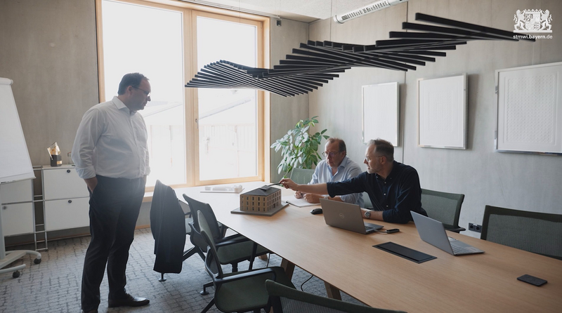 Drei Preisträger des Bayerischen Energiepreises stehen um einen Tisch in einem Büro