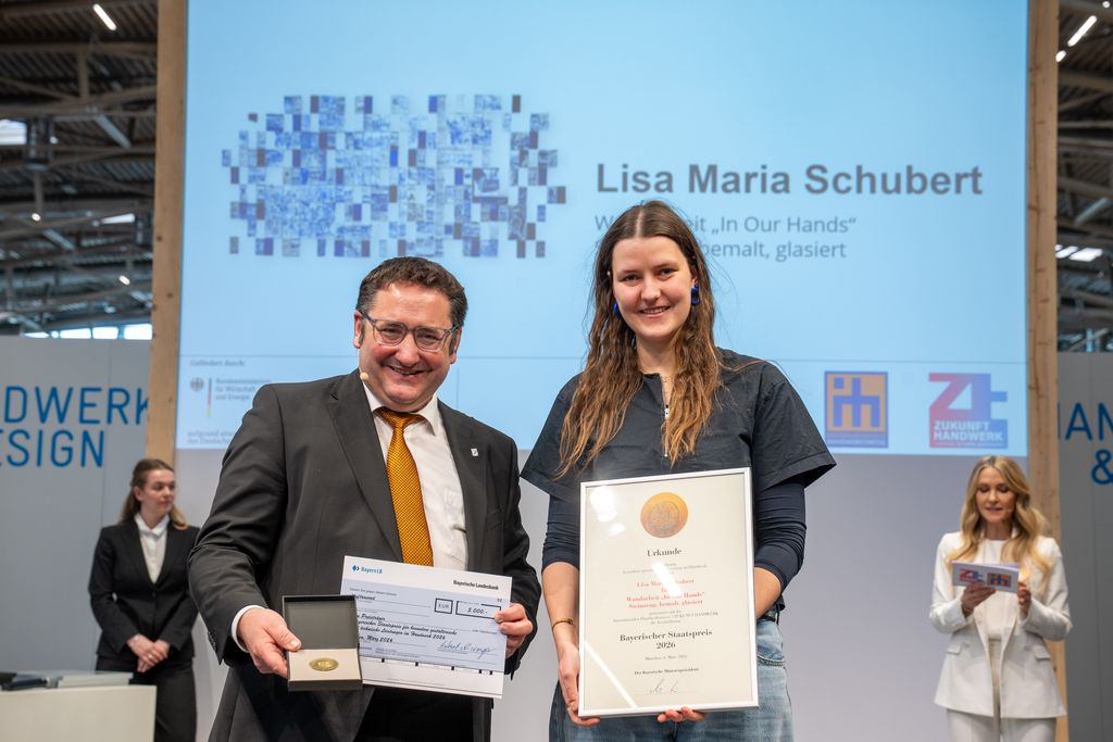 Bayerns Wirtschaftsstaatssekretär Tobias Gotthardt übergibt den Staatspreis an Lisa Maria Schubert.