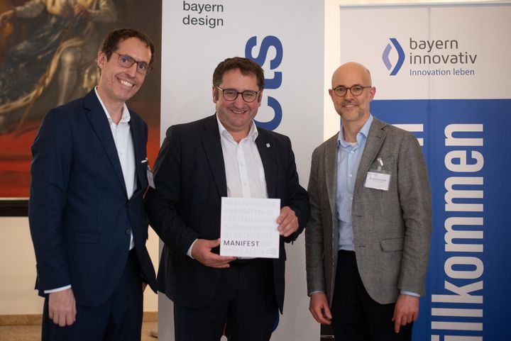 Dr. Kilian Steiner, Leiter der Öffentlichkeitsarbeit bei bayern design (links), und Dr. Henning Berthold, Leiter Kreativwirtschaft bei Bayern Innovativ (rechts), überreichen Staatssekretär Tobias Gotthardt das Manifest.
Foto: Linus Rapp &amp; bayern design