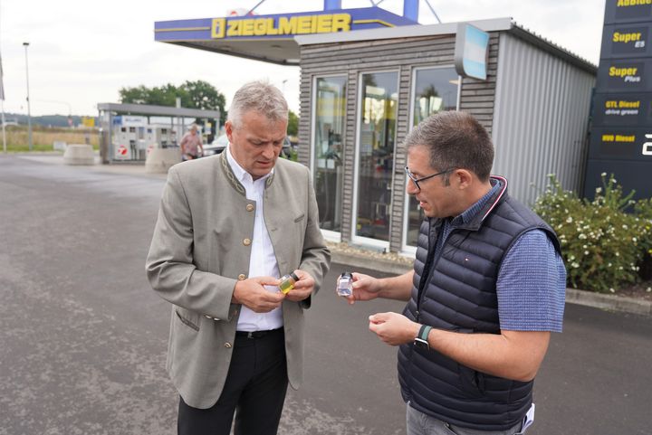 Nico Zieglmeier zeigt Wirtschaftsstaatssekretär Roland Weigert (l.) Proben von HVO100 und von herkömmlichem Diesel. Foto: StMWi
