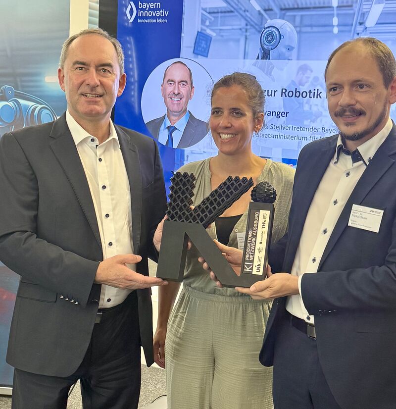Bayerns Wirtschaftsminister Hubert Aiwanger ruft Unternehmen auf, die Chancen von Automatisierung und Robotik zu nutzen. Professor Dr. Markus Sause (Leiter KI-Produktionsnetzwerk) und Dr. Juliane Gottmann (Geschäftsführerin des Zentrums für Produktion der Zukunft) überreichten ein KI-Präsent.